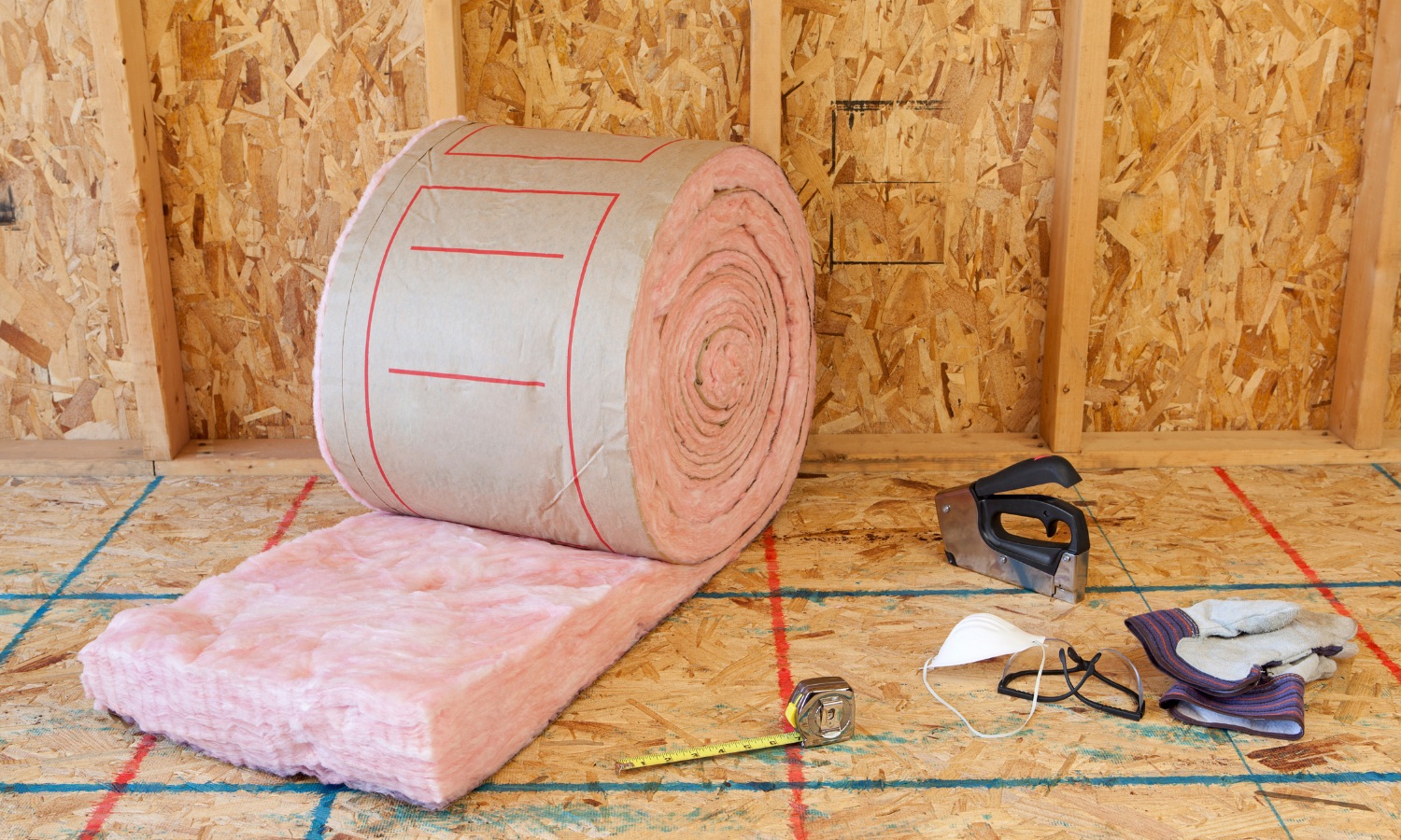 A roll of pink insulation material and various tools on a wooden floor inside a construction site, highlighting Bayside Builders Group's commitment to quality home renovations in the Bay Area.