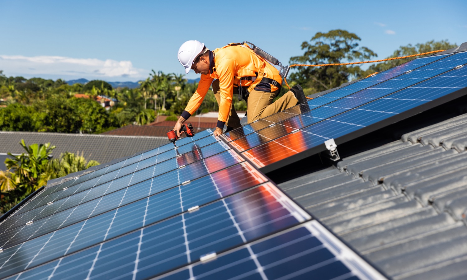 A construction worker in safety gear installs solar panels on a rooftop, showcasing Bayside Builders Group's commitment to sustainable home improvements in the Bay Area.